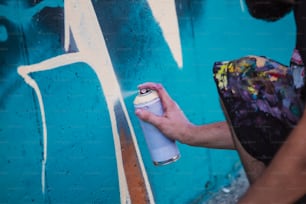 Street artist painting colorful graffiti on generic wall - Modern art concept with urban guy performing and preparing live murales with multi color aerosol spray