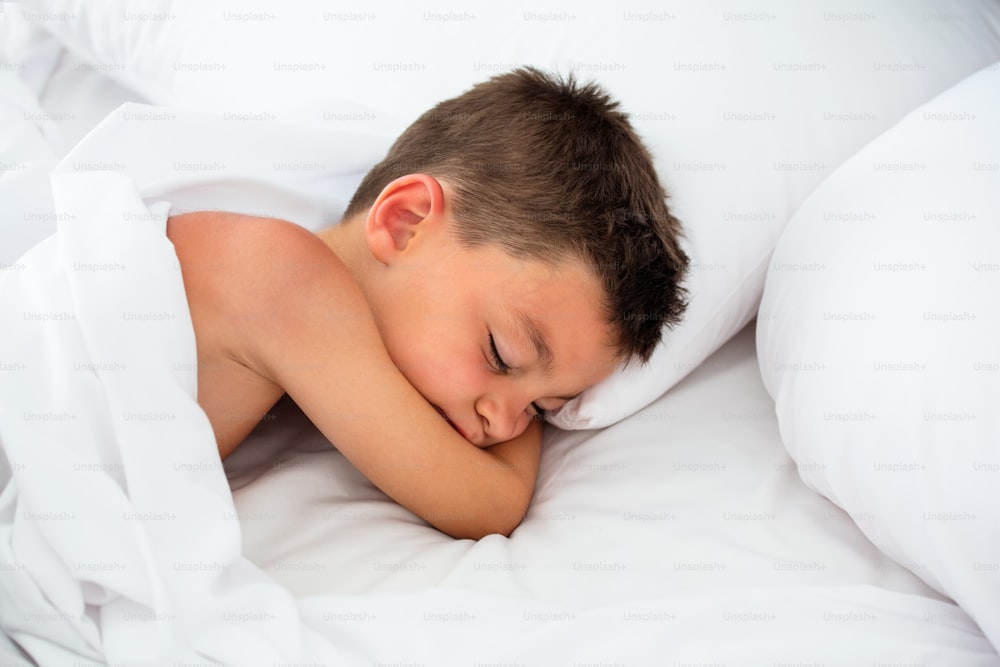 Adorable little boy sleeping in bed. Cute little boy sleeping in white bed. people, children, rest and comfort concept. Soft focus. Copy space.