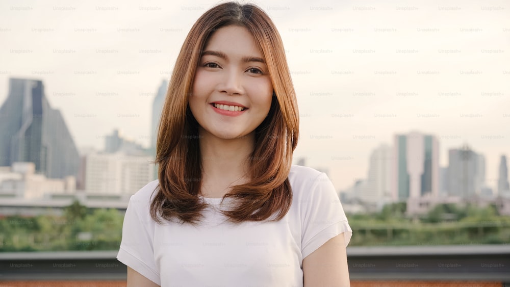 Cheerful beautiful young Asian woman feeling happy smiling to camera while traveling on the street at downtown city. Lifestyle backpack tourist travel holiday concept. Portrait looking at camera.