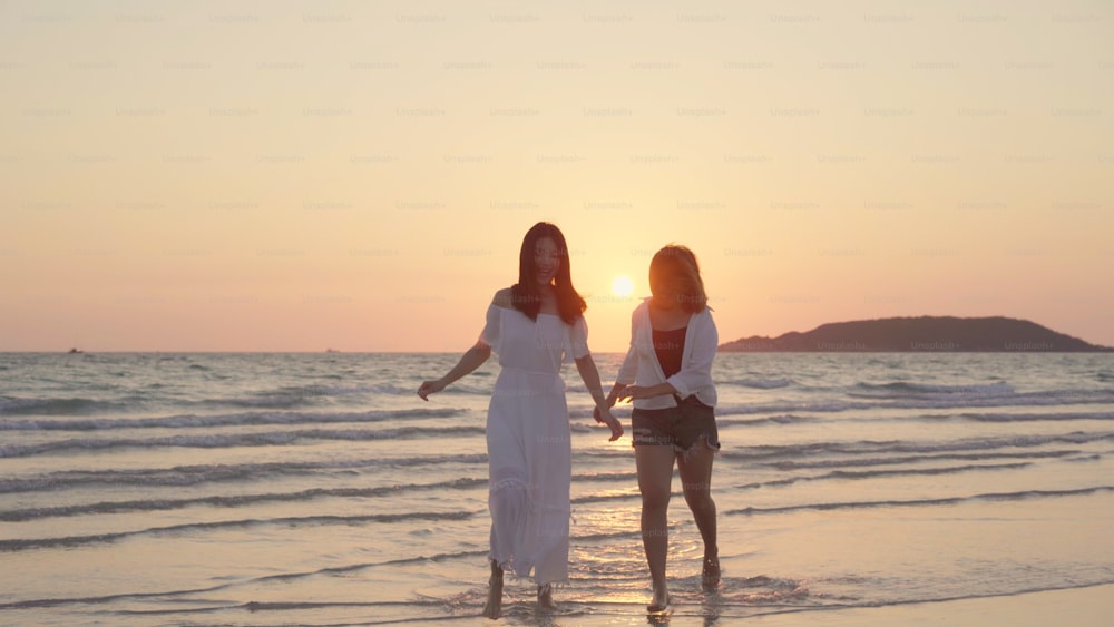 Junges asiatisches lesbisches Paar läuft am Strand. Schöne Frauen Freunde glücklich entspannen sich Spaß am Strand in der Nähe des Meeres, wenn Sonnenuntergang am Abend. Lifestyle lesbisches Paar Reisen am Strand Konzept.