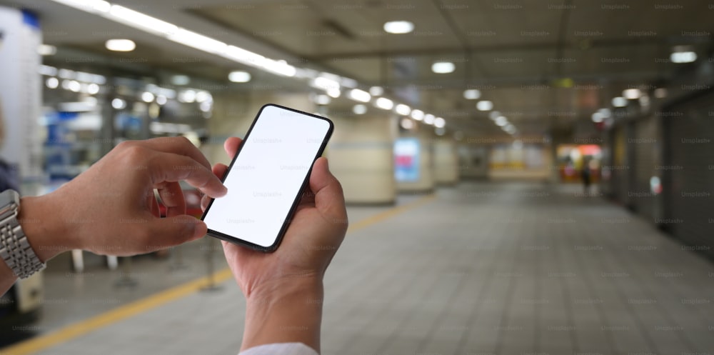 Close-up view of young man touching blank screen smartphone at railway station, blurred background