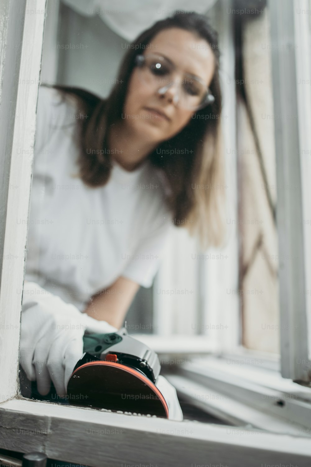Beautiful and diligent middle age handy woman renovating her old home or apartment. She is holding professional grinder and brushing old window for later painting. Do it yourself housework concept.