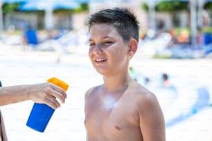 Young boy sitting on the beach during his summer vacation having sunscreen applied by a parent to prevent burning from harmful UV rays