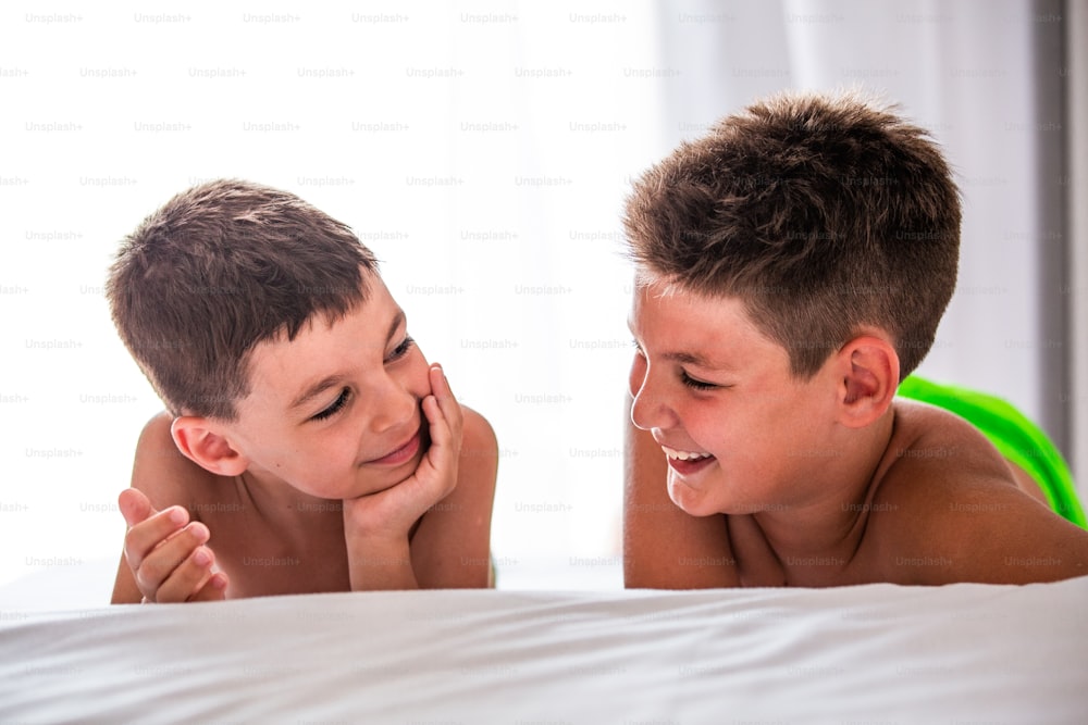 Dos lindos niños acostados en la cama y mirándose. Hermosos niños sonriendo y jugando en la cama antes de acostarse.