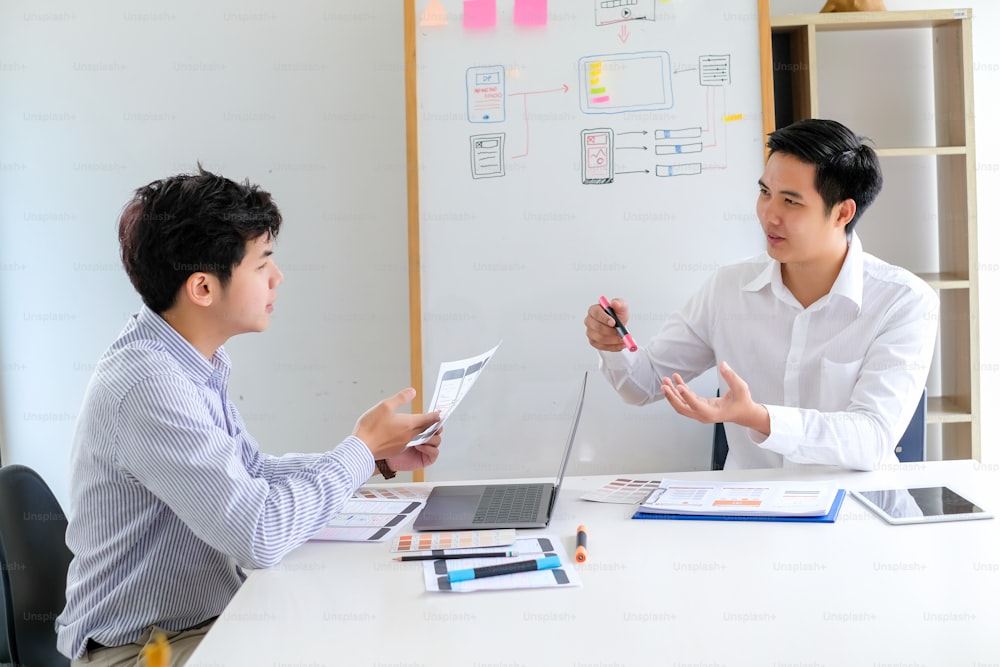 Due uomini asiatici stanno lavorando insieme per progettare siti Web e applicazioni sul telefono cellulare.