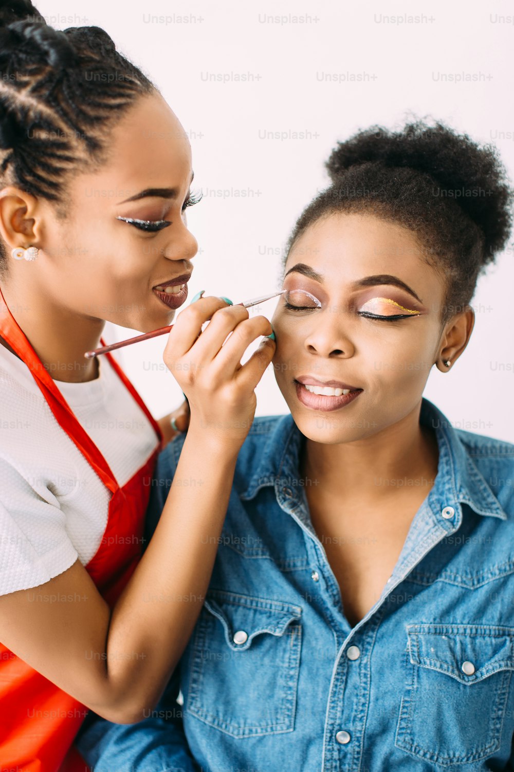 Mulher afro-americana bonita jovem que aplica maquiagem pelo maquiador