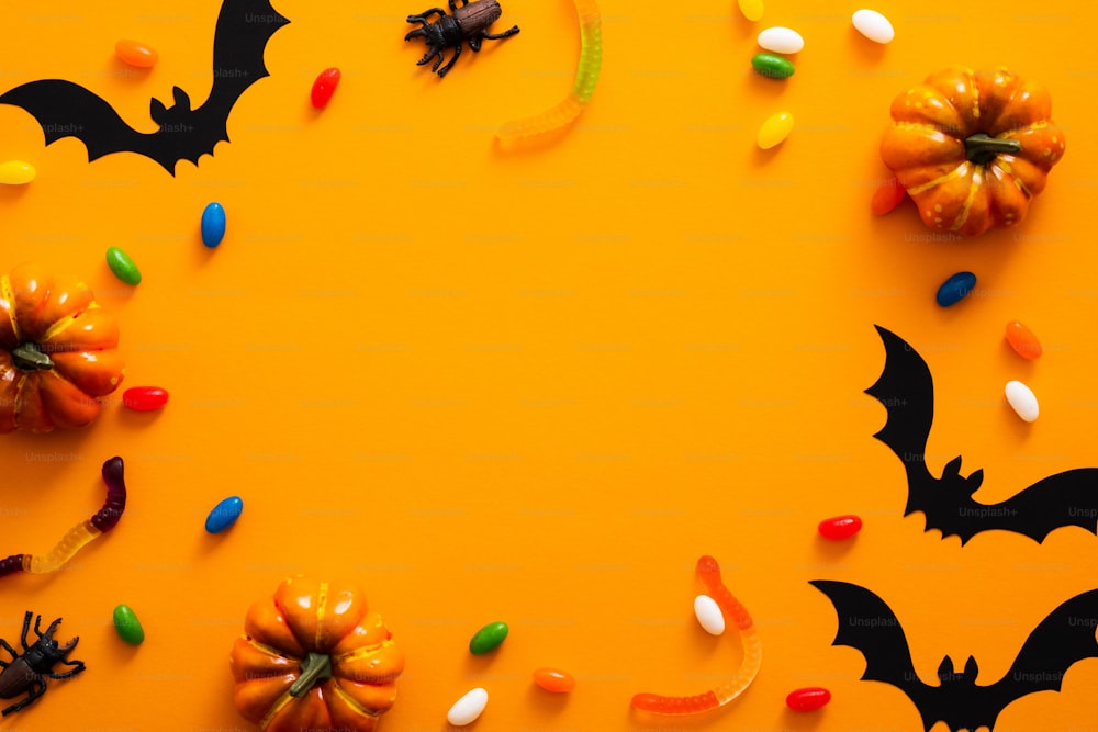 Feliz conceito de feriado de halloween. Decorações de Halloween, abóboras, morcegos, doces, insetos no fundo laranja. Maquete de cartão de felicitações da festa de Halloween com espaço de cópia. Flat lay, vista superior, sobrecarga.