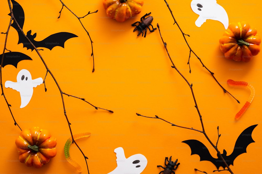 Happy halloween holiday concept. Halloween decorations, pumpkins, bats, candy, ghosts, bugs on orange background. Halloween party greeting card. Flat lay, top view, overhead.