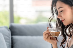 Asian young woman drinks coffee in the morning while sitting on sofa couch.