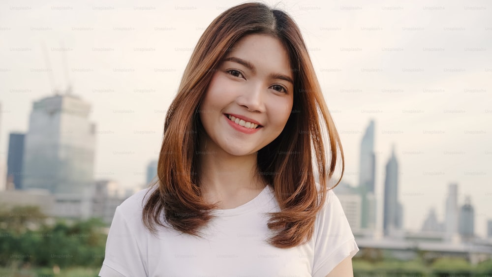 Cheerful beautiful young Asian woman feeling happy smiling to camera while traveling on the street at downtown city. Lifestyle backpack tourist travel holiday concept. Portrait looking at camera.