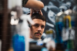 Close up foto de homem recebendo corte de cabelo da moda na barbearia. Cabeleireiro masculino atendendo cliente, fazendo corte de cabelo usando máquina e pente.