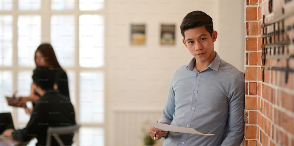 Young businessman looking confidently at the camera while standing in modern office room