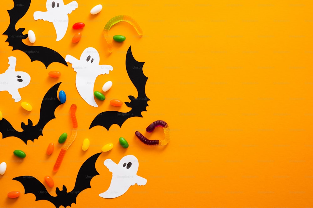 Happy halloween holiday concept. Halloween decorations, bats, ghosts, candy on orange background. Halloween party greeting card mockup with copy space. Flat lay, top view, overhead.