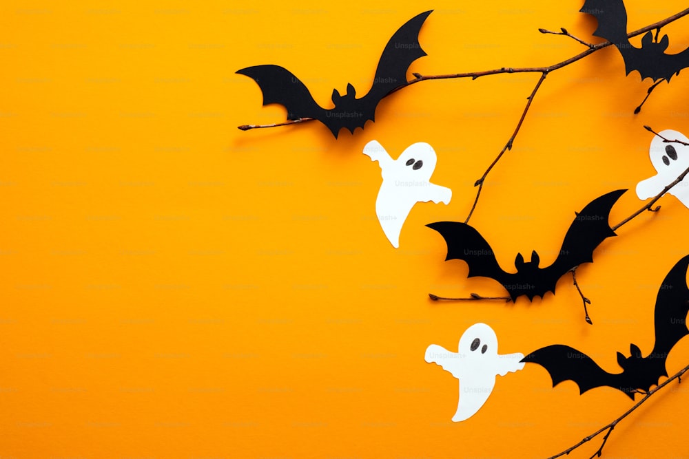 Concepto de feliz día de Halloween. Decoraciones de Halloween, fantasmas de papel, murciélagos sobre fondo naranja. Plano plano, vista superior, espacio de copia.