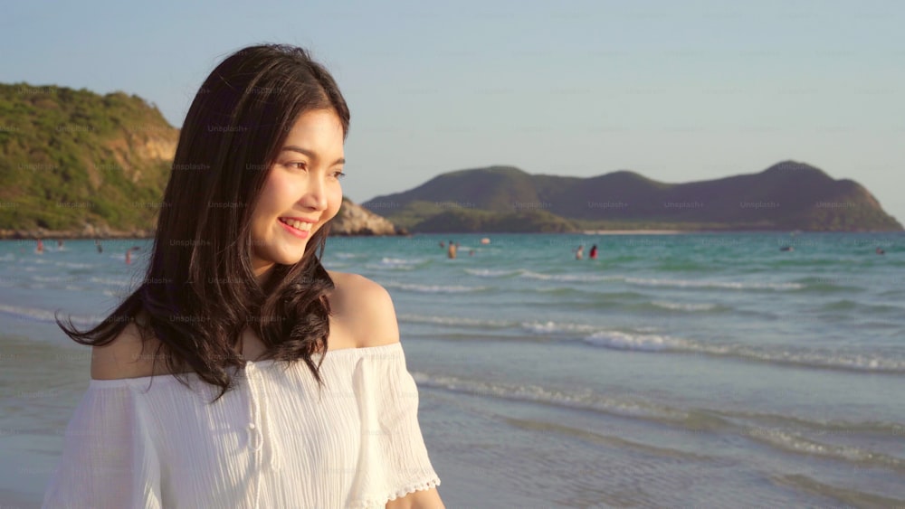 Mulher asiática nova que caminha na praia. Bela fêmea feliz relaxar andando na praia perto do mar quando o pôr do sol à noite. Estilo de vida das mulheres viajam na praia.