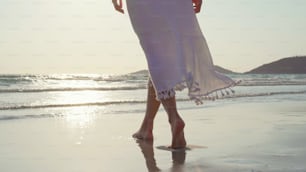 Mulher asiática nova que caminha na praia. Bela fêmea feliz relaxar andando na praia perto do mar quando o pôr do sol à noite. Estilo de vida das mulheres viajam na praia.