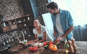 Romantic couple is cooking on kitchen. Handsome man and attractive young woman are having fun together while making salad. Healthy lifestyle concept.