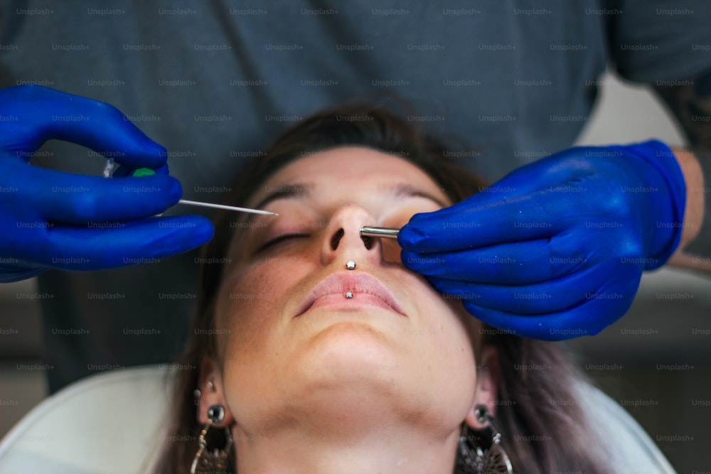 Portrait d’une femme se faisant percer le nez. Homme montrant un processus de perçage du nez avec des gants stériles en latex. Procédure de perçage des narines