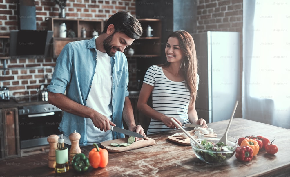 Pareja romántica está cocinando en la cocina. Un hombre guapo y una joven atractiva se divierten juntos mientras preparan ensalada. Concepto de estilo de vida saludable.