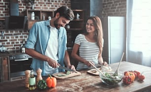 Romantic couple is cooking on kitchen. Handsome man and attractive young woman are having fun together while making salad. Healthy lifestyle concept.