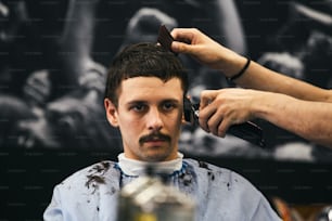 Mann bekommt trendigen Haarschnitt im Friseurladen. Männlicher Friseur, der den Kunden bedient und Haarschnitt mit Maschine und Kamm macht.