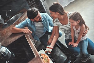 Mom, dad and daughter are cooking on kitchen. Happy family concept. Handsome man, attractive young woman and their cute little daughter are making pizza together.