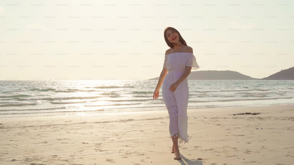 Junge asiatische Frau spazieren am Strand. Schöne weibliche glückliche Entspannung am Strand in der Nähe des Meeres bei Sonnenuntergang am Abend. Lifestyle-Frauen reisen am Strandkonzept.