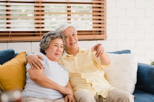 Coppia di anziani asiatici che guardano la televisione nel soggiorno di casa, dolce coppia si gode il momento d'amore mentre è sdraiata sul divano quando si rilassa a casa. Godersi il tempo di vita della famiglia anziana a casa concetto.