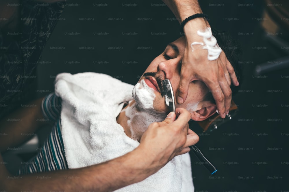 Navalha nas mãos do barbeiro especialista. Barbeiro raspando um homem em uma barbearia, close-up. Homem mith bigodes tendo um barbear