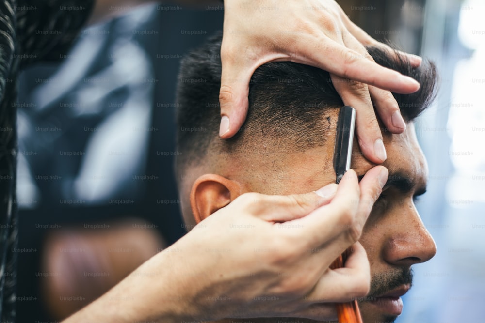 Navalha nas mãos do barbeiro profissional. Cabeleireiro raspando o cabelo do homem com uma navalha reta