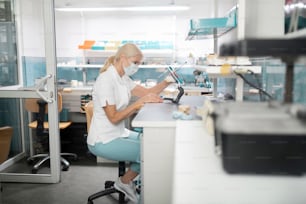 Prosthetic technician. Concentrated dental technician wearing mask sitting at her table working on cast model of patients teeth.