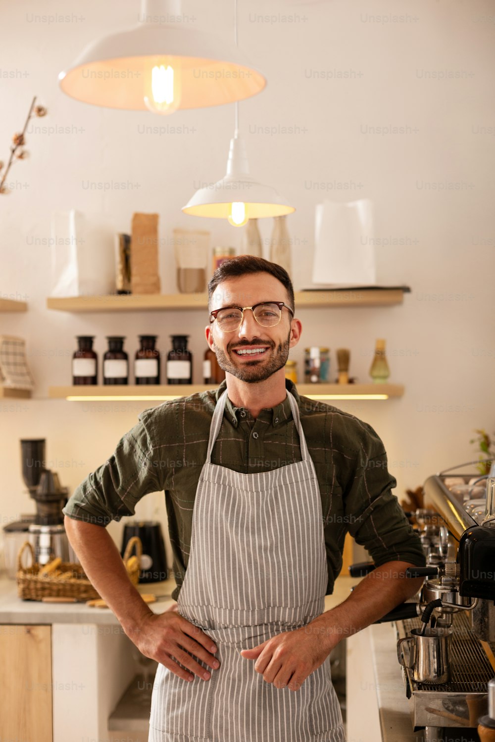 ハンサムな起業家。コーヒーマシンの近くに立っているコーヒーショップを所有するハンサムな若い起業家