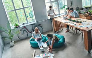 Gruppo di giovani uomini d'affari stanno lavorando insieme in un ufficio moderno. Persone creative con laptop, tablet, smartphone, notebook. Team hipster di successo nel coworking. Liberi professionisti.