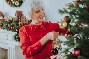 Anciana positiva de pie cerca del árbol de Navidad en casa foto de archivo