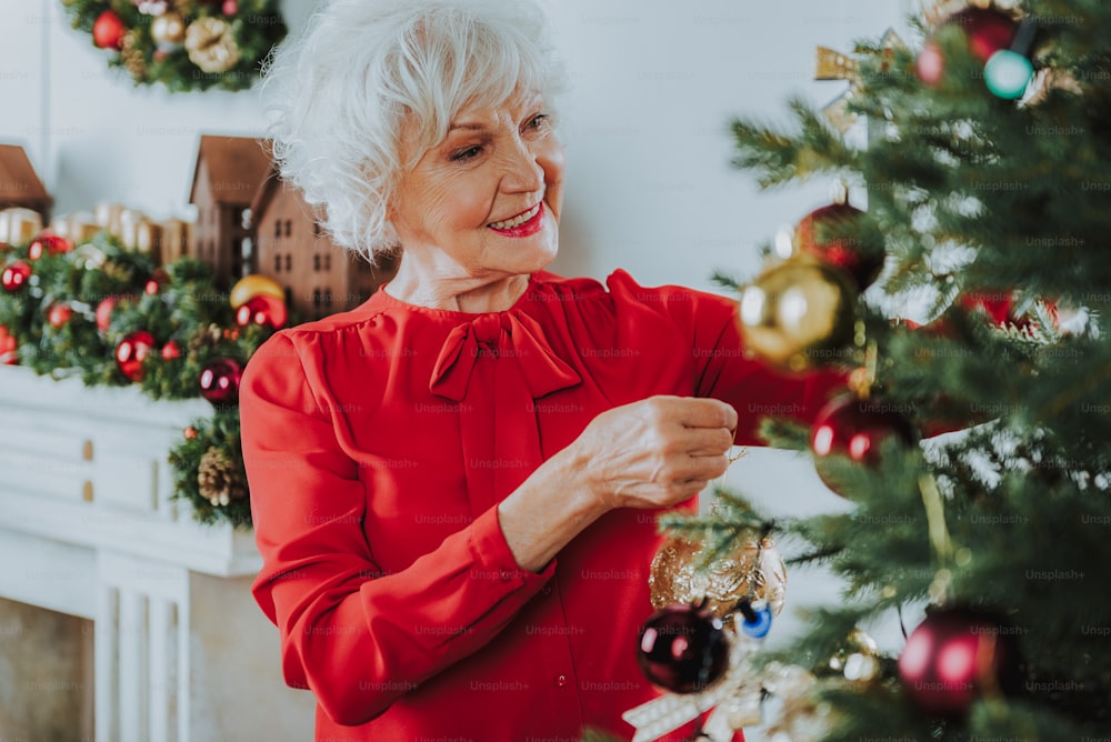 Positive old lady standing near Christmas tree at home stock photo
