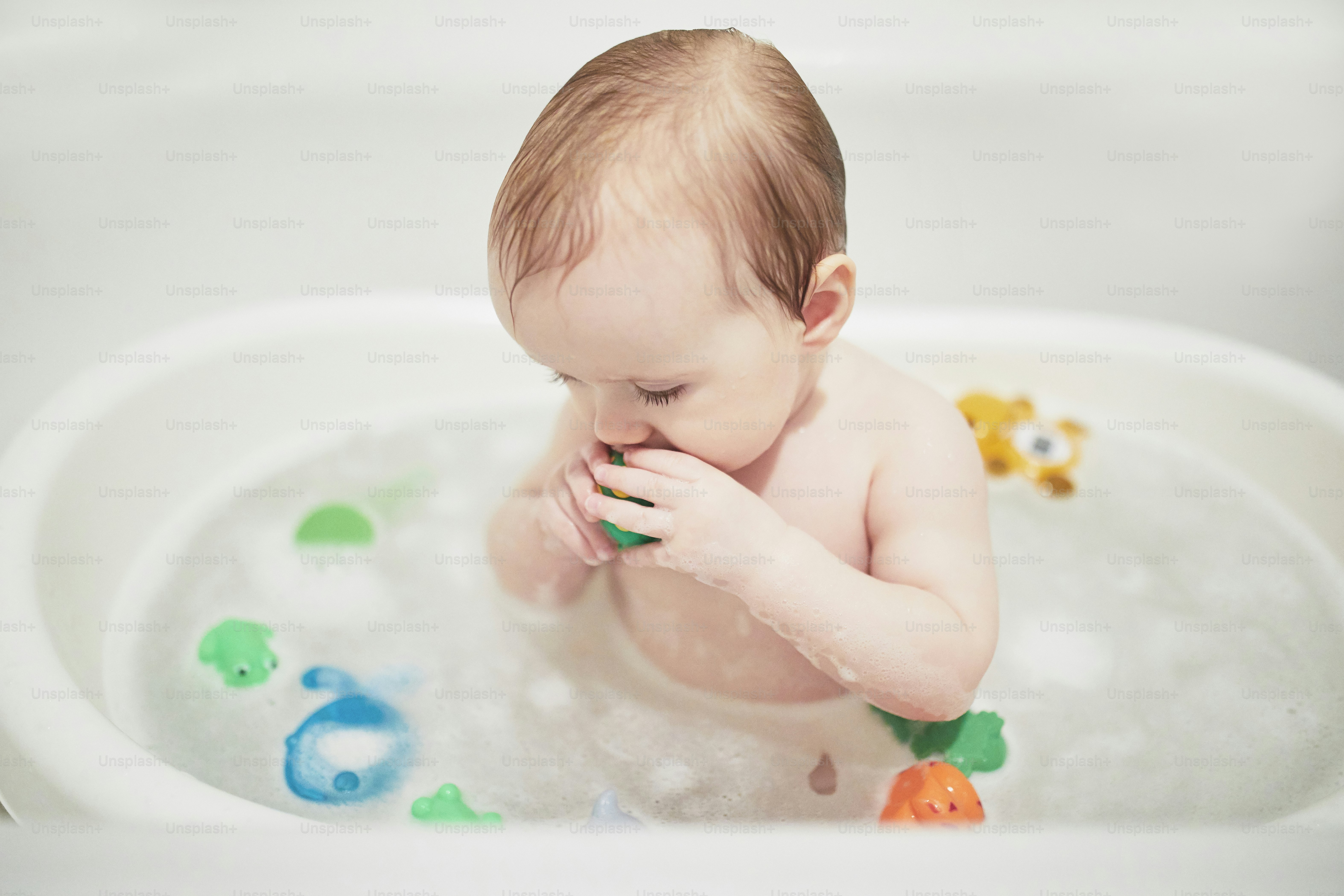 Cute little girl playing with rubber toys in small bathtub. Happy kid having fun while bathing