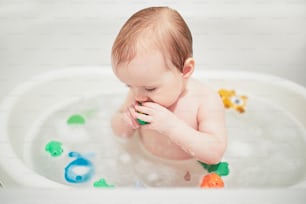 Linda niña jugando con juguetes de goma en una bañera pequeña. Niño feliz divirtiéndose mientras se baña