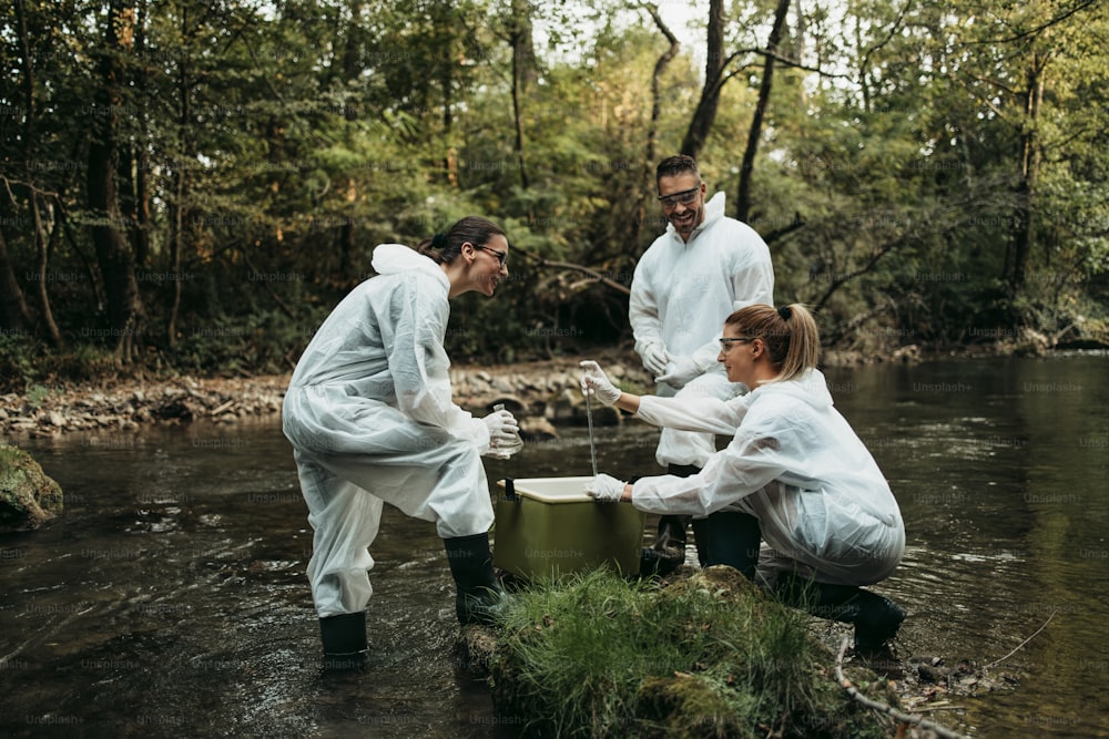 Scientists biologists and researchers in protective suits taking water samples from polluted river.