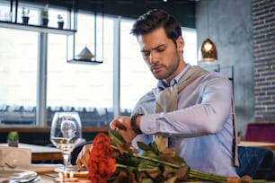 Portrait of man with bouquet of roses looking at his watch while waiting for a girlfriend that is late. Romantic dinner concept. Horizontal shot