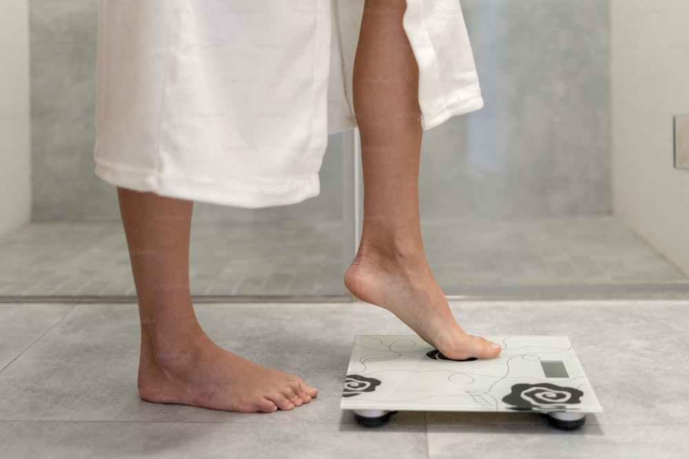 Cropped view of woman in white and comfort bathrobe making step on weigher in bathroom with copy space