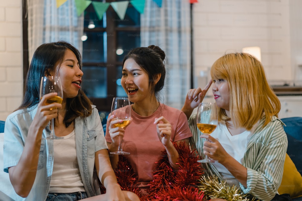 Group of Asian women party at home, female drinking cocktail talking having funny together on sofa in living room in night. Teenager young friend play game, friendship, celebrate holiday concept.