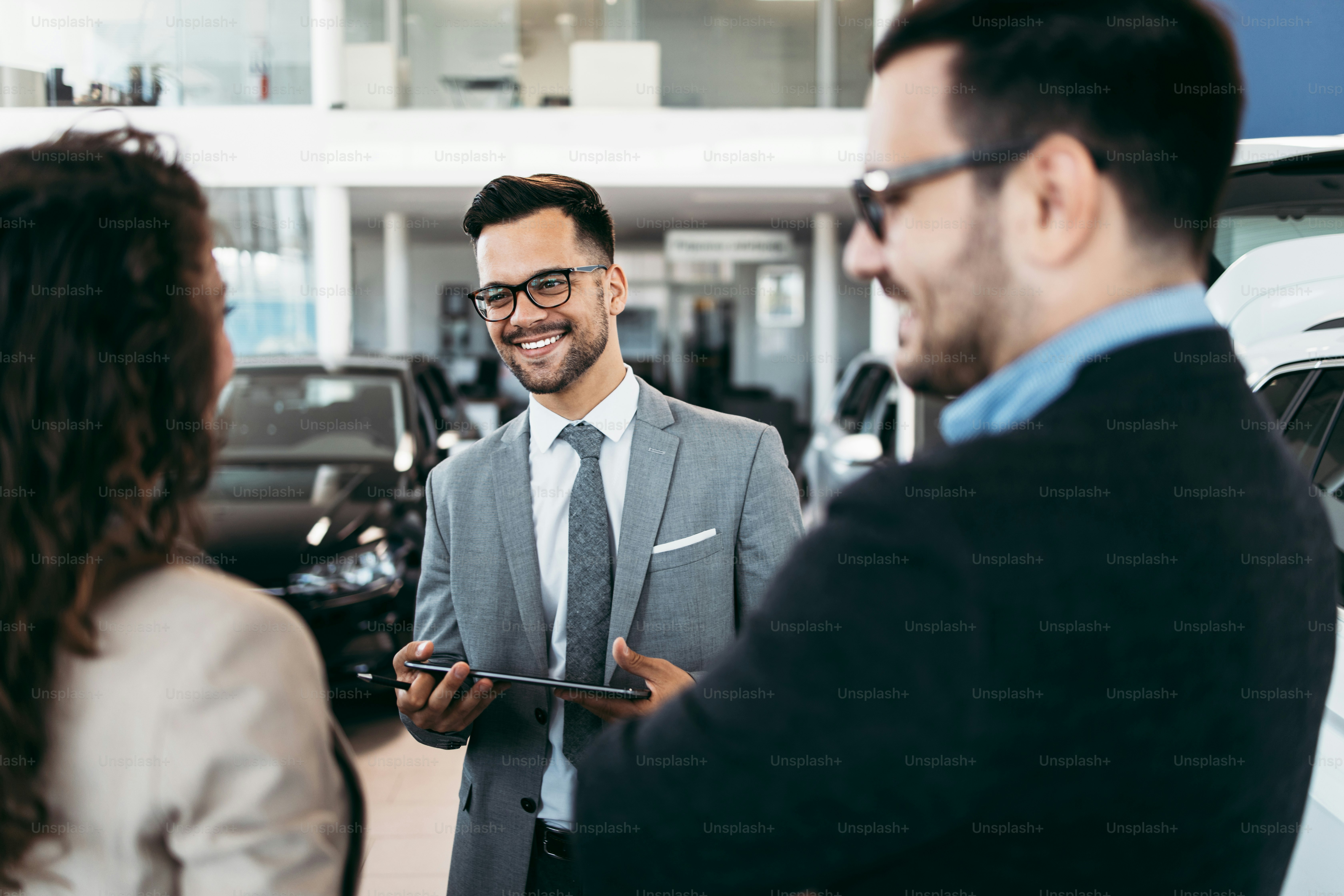Middle age couple choosing and buying car at car showroom. Car salesman helps them to make right decision.