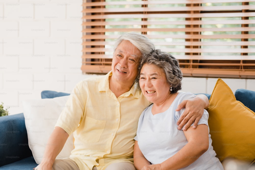 Asian elderly couple watching television in living room at home, sweet couple enjoy love moment while lying on the sofa when relaxed at home. Enjoying time lifestyle senior family at home concept.