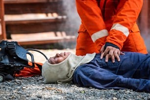 安全救助任務中の消防服を着た消防士のミディアムショットは、応急処置の緊急CPRによって燃えている敷地内で心臓発作の男性の呼吸を止めるのに役立ちます。安全、救助、ヘルスケアのコンセプト。