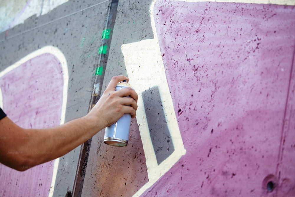 Artista callejero pintando graffiti colorido en pared genérica - Concepto de arte moderno con chico urbano que realiza y prepara murales en vivo con aerosol multicolor spray