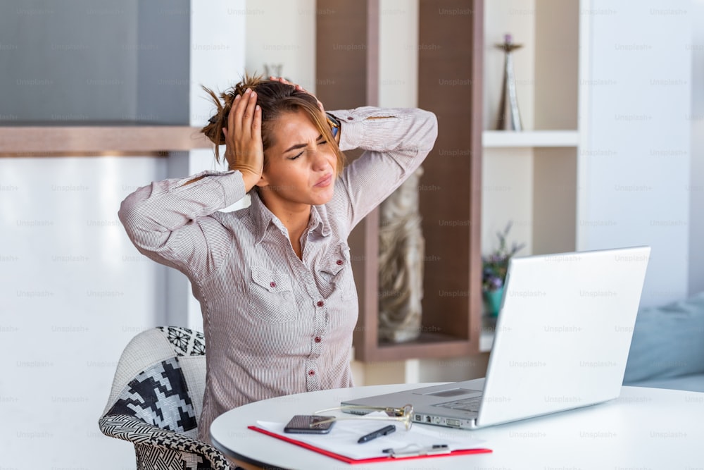 Young frustrated woman working at office desk in front of laptop suffering from chronic daily headaches, treatment online, appointing to a medical consultation, electromagnetic radiation, sick pay