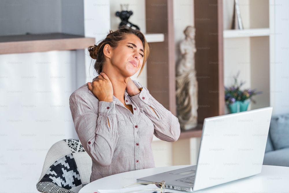 Feeling exhausted. Frustrated young woman looking exhausted and massaging her neck while sitting at his working place