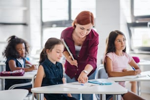 A friendly teacher walking among small school children on the lesson, explaining and helping.