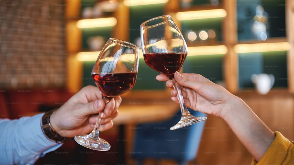 Primer plano de manos masculinas y femeninas sosteniendo copas de vino tinto. Concepto de cena romántica. Disparo horizontal
