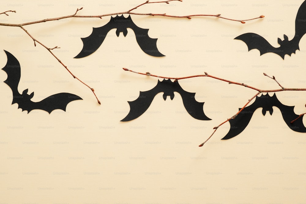 Halloween paper decorations on pastel beige background. Black bats sitting on branch. Halloween concept. Flat lay, top view, copy space